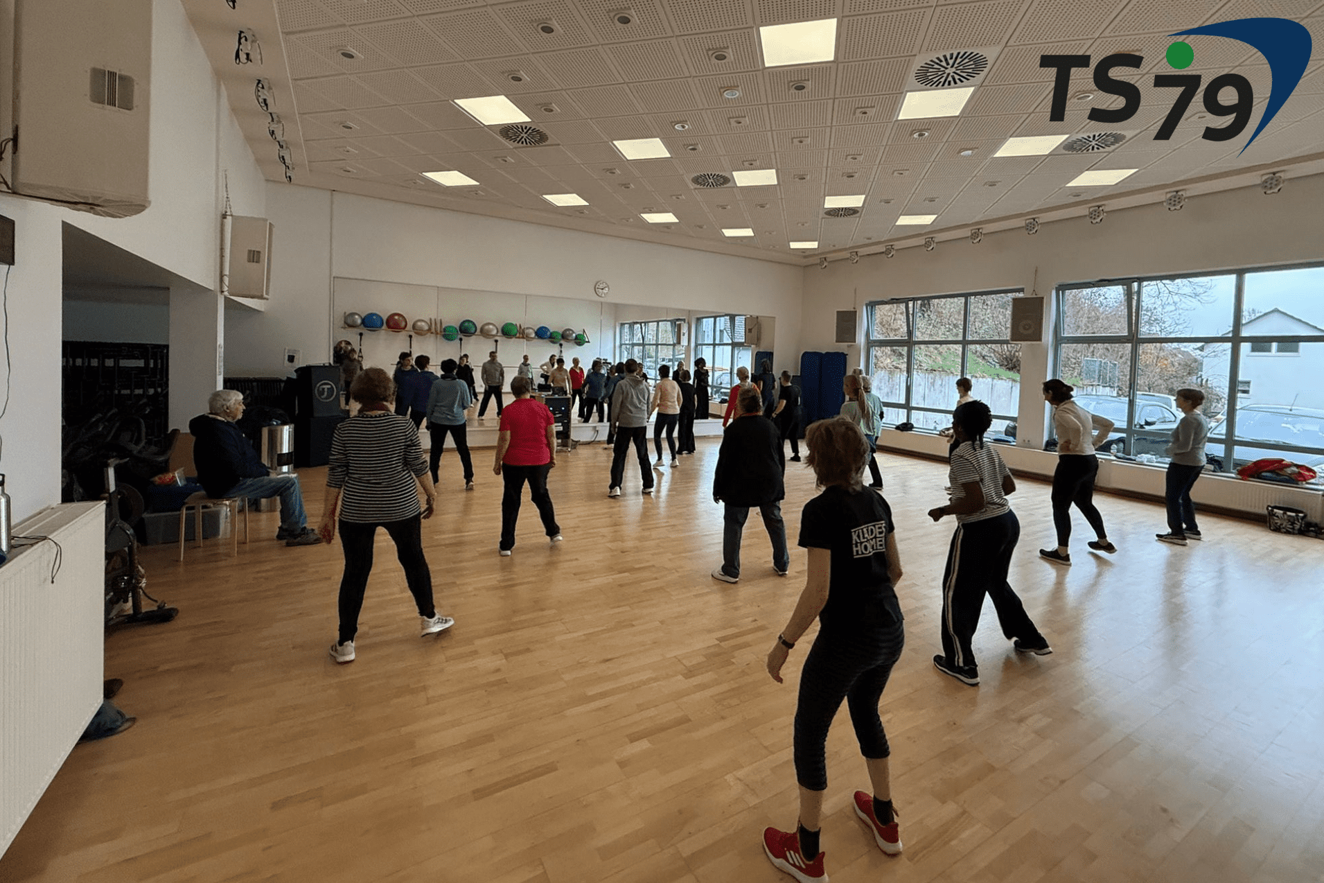 Gruppentraining in einem hellen Raum mit vielen Teilnehmern, die gemeinsam Übungen durchführen.