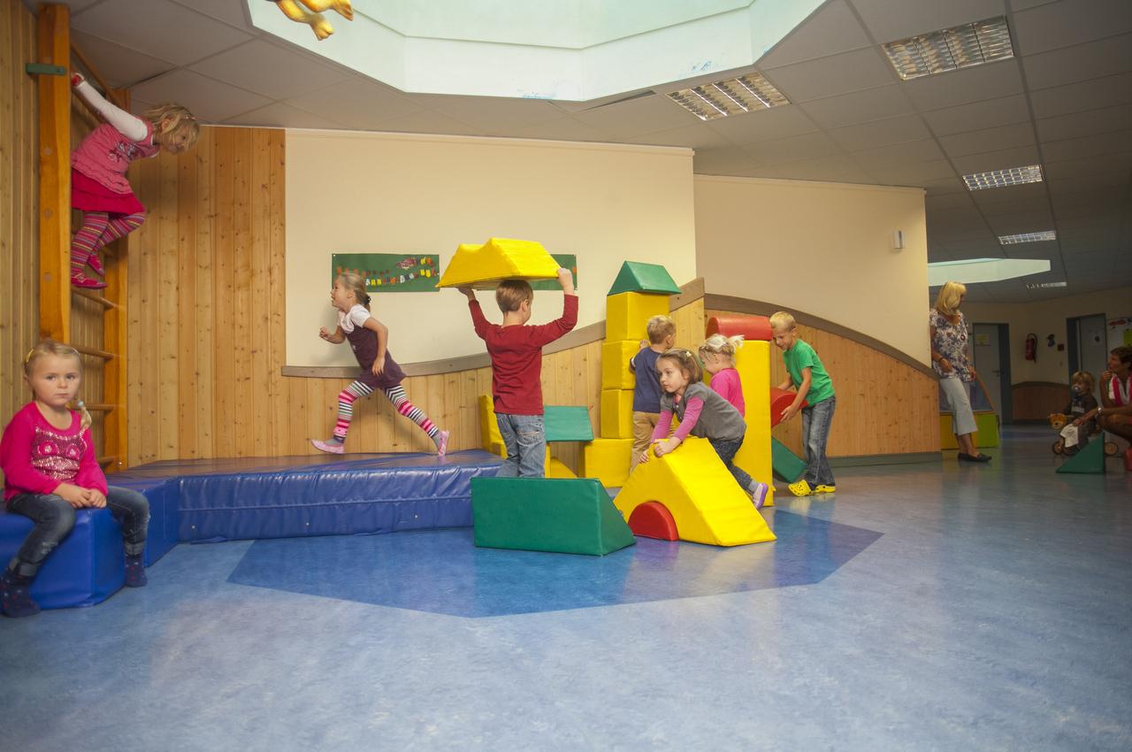 Kinder spielen in einem hellen Spielzimmer mit bunten Kletterelementen und Softspielzeug.