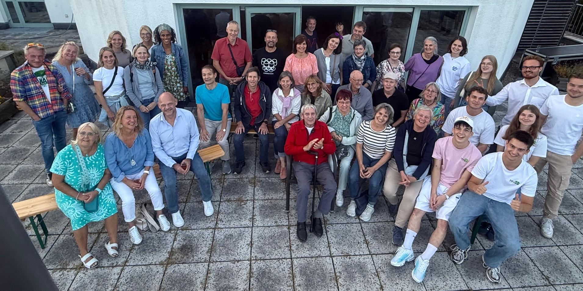 Gruppenfoto von 42 Personen auf einer Terrasse vor einem modernen Gebäude, lächelnd und in entspannter Atmosphäre.